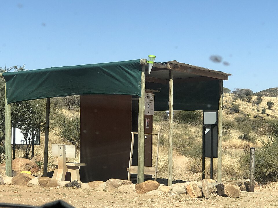 A rain gauge beside a roofed structure at Avis Dam, Namibia. This context scene illustrates why nearby shelter and runoff deserve inspection, not an ideal mounting recommendation.